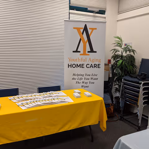 Indoor registration table with yellow cloth and Youthful Aging Home Care banner.