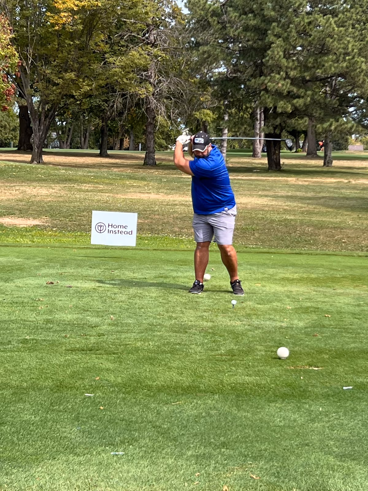 Man swings golf club on a green with a Home Instead sign nearby