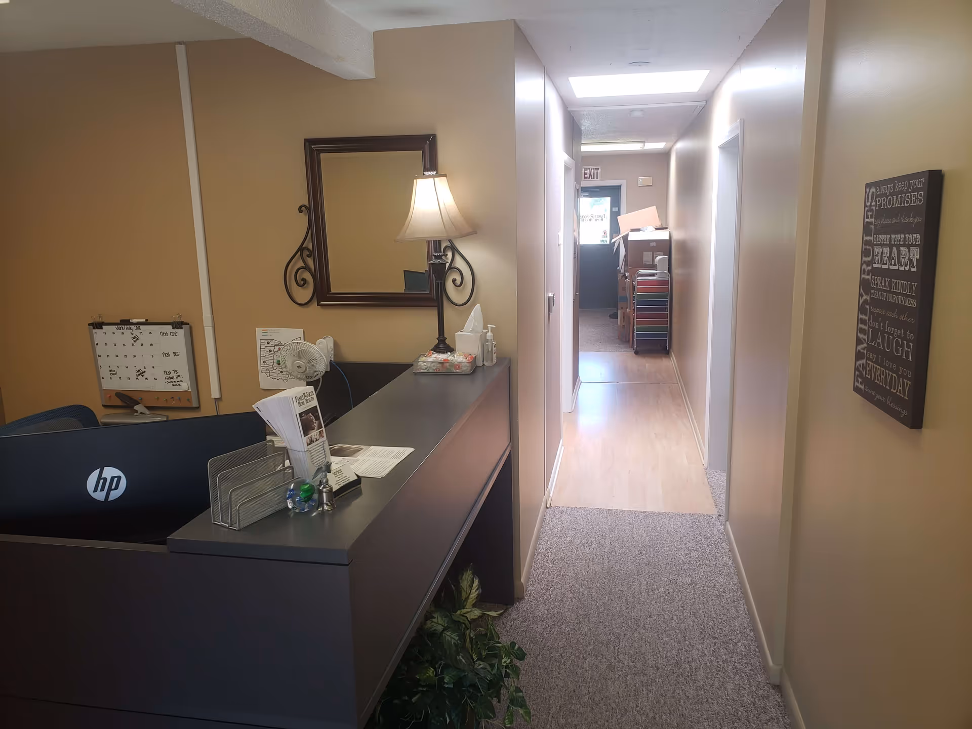 Reception desk sits in a hallway of a senior living facility with a lamp and mirror