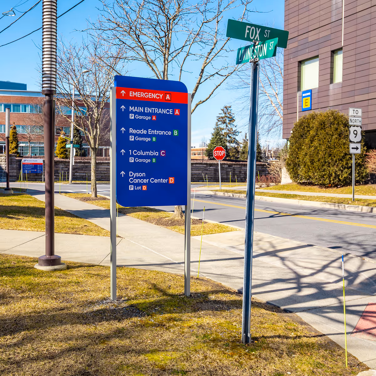 Blue informational sign with street signs beside a brick building outdoors