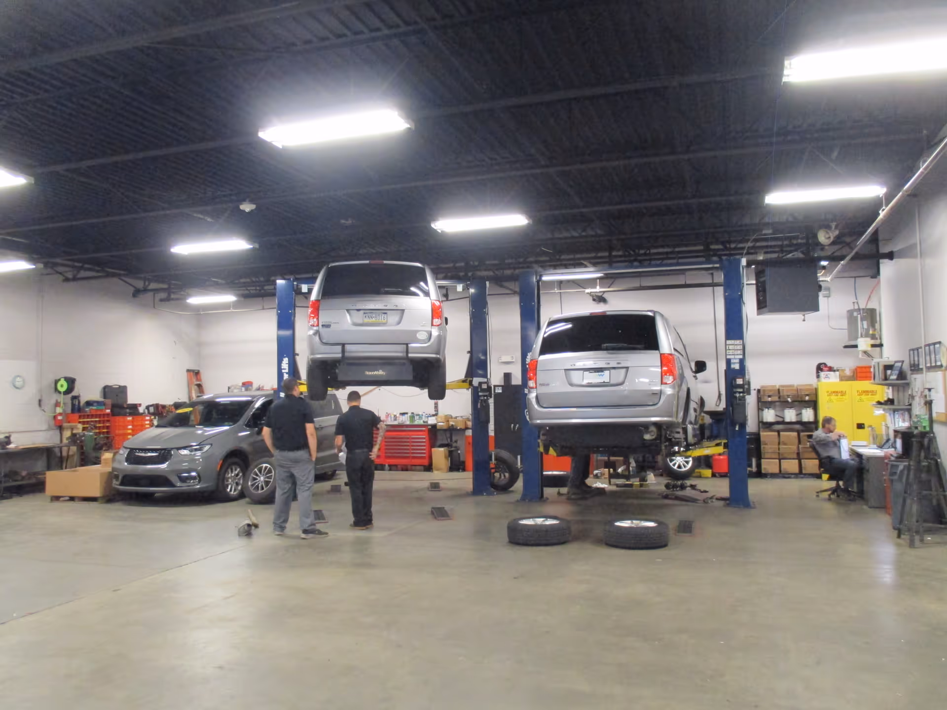 An auto repair shop interior with two vehicles elevated on lifts and technicians working.