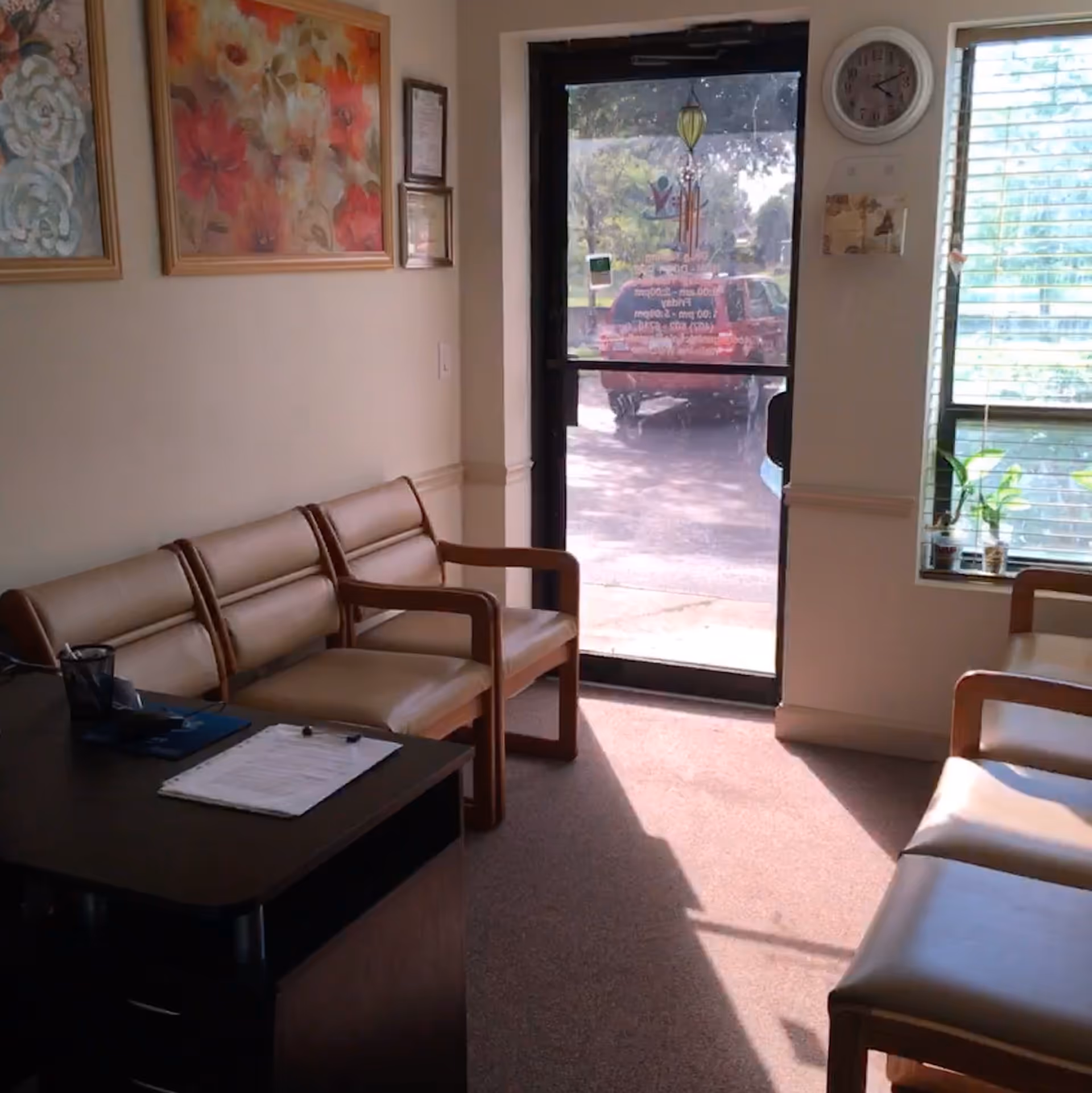Interior waiting area with beige chairs, a desk with papers, and a glass exit door.