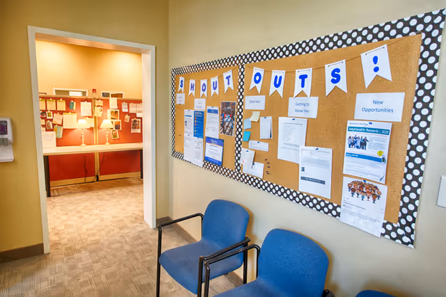 Interior hallway with blue chairs and a bulletin board labeled SHOUT OUTS.