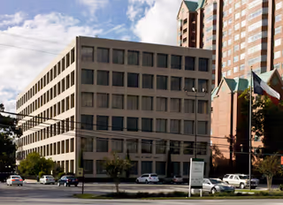 Exterior view of a beige, multi-story building with cars parked in front.