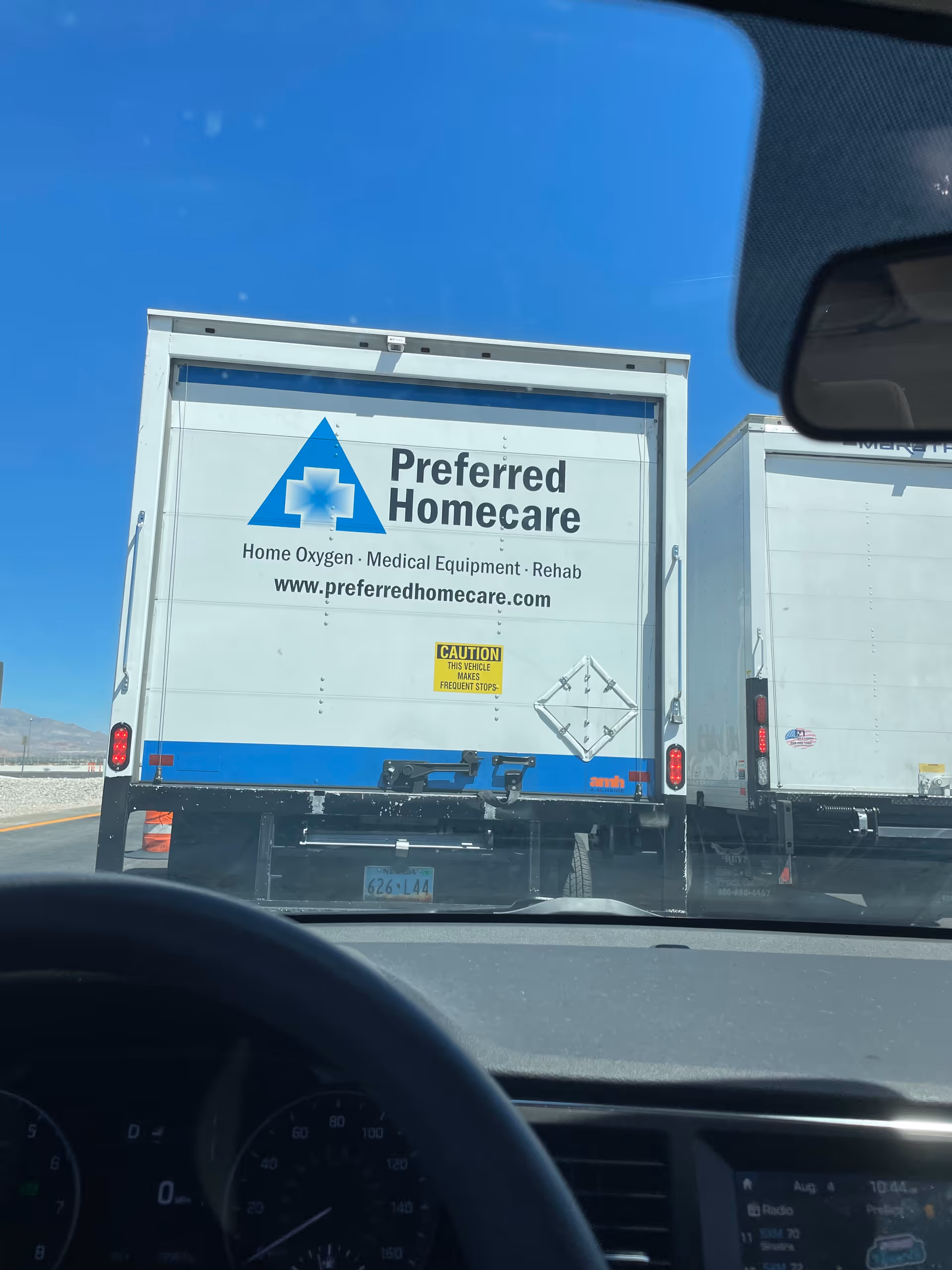 Rear view from inside a car of Preferred Homecare delivery trucks on a highway.
