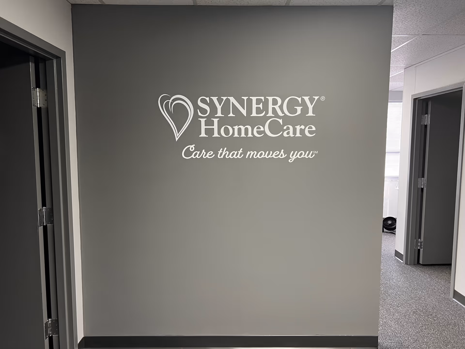 Gray interior hallway wall with SYNERGY HomeCare logo and slogan.