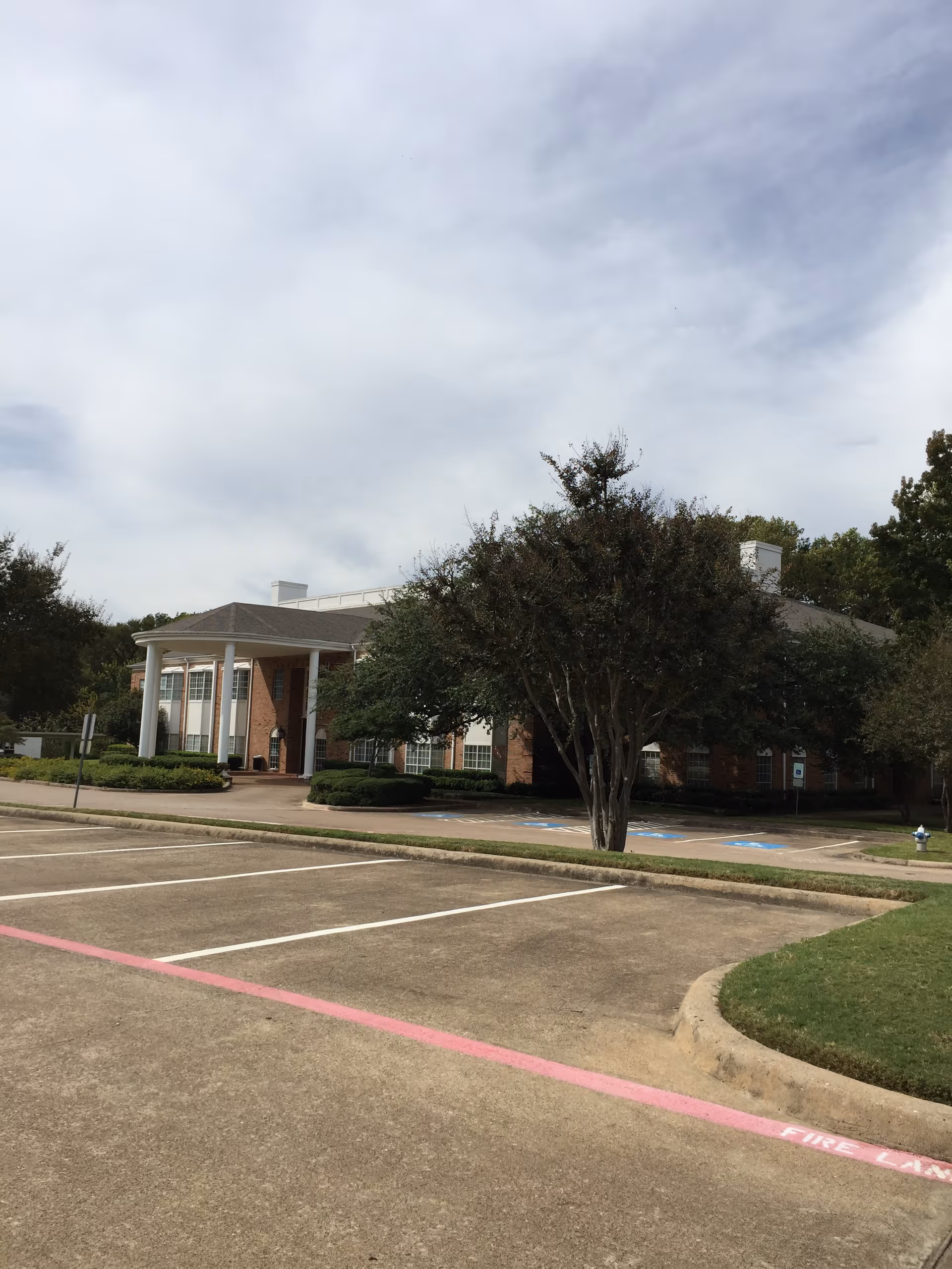A senior living facility's brick exterior with a covered entrance and parking lot.