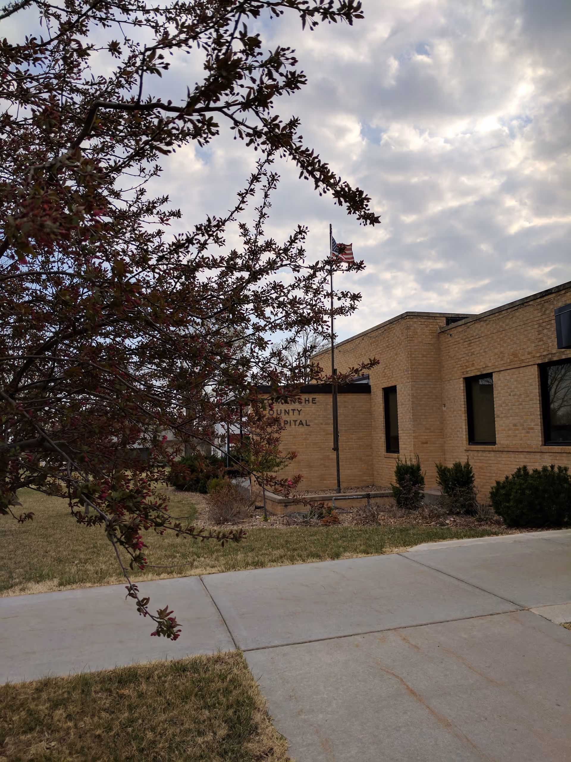 Exterior of Comanche County Hospital with flagpole and foreground tree.