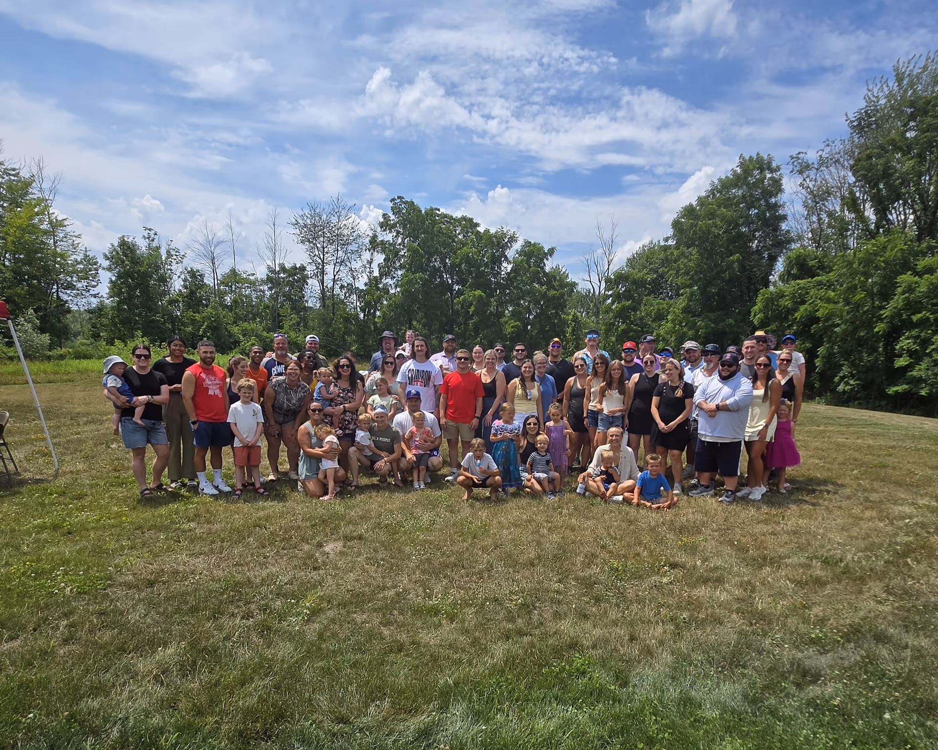Large group photo of residents and staff outdoors on a grassy field with trees.