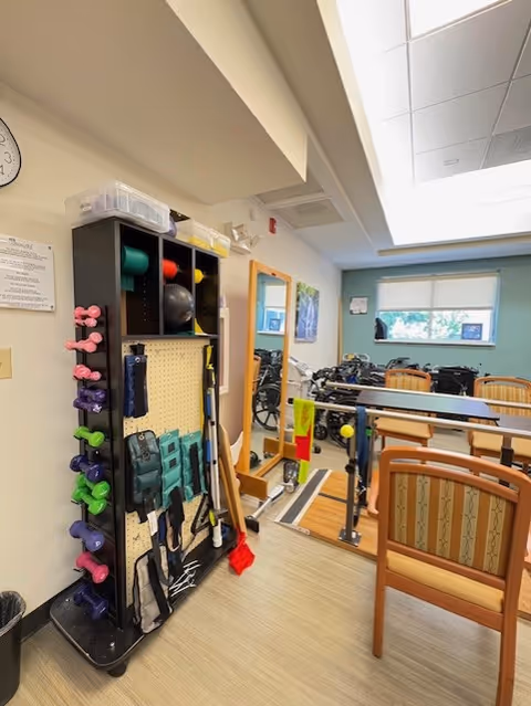 Interior rehab gym corner with a dumbbell rack, bands, and exercise equipment near seating.