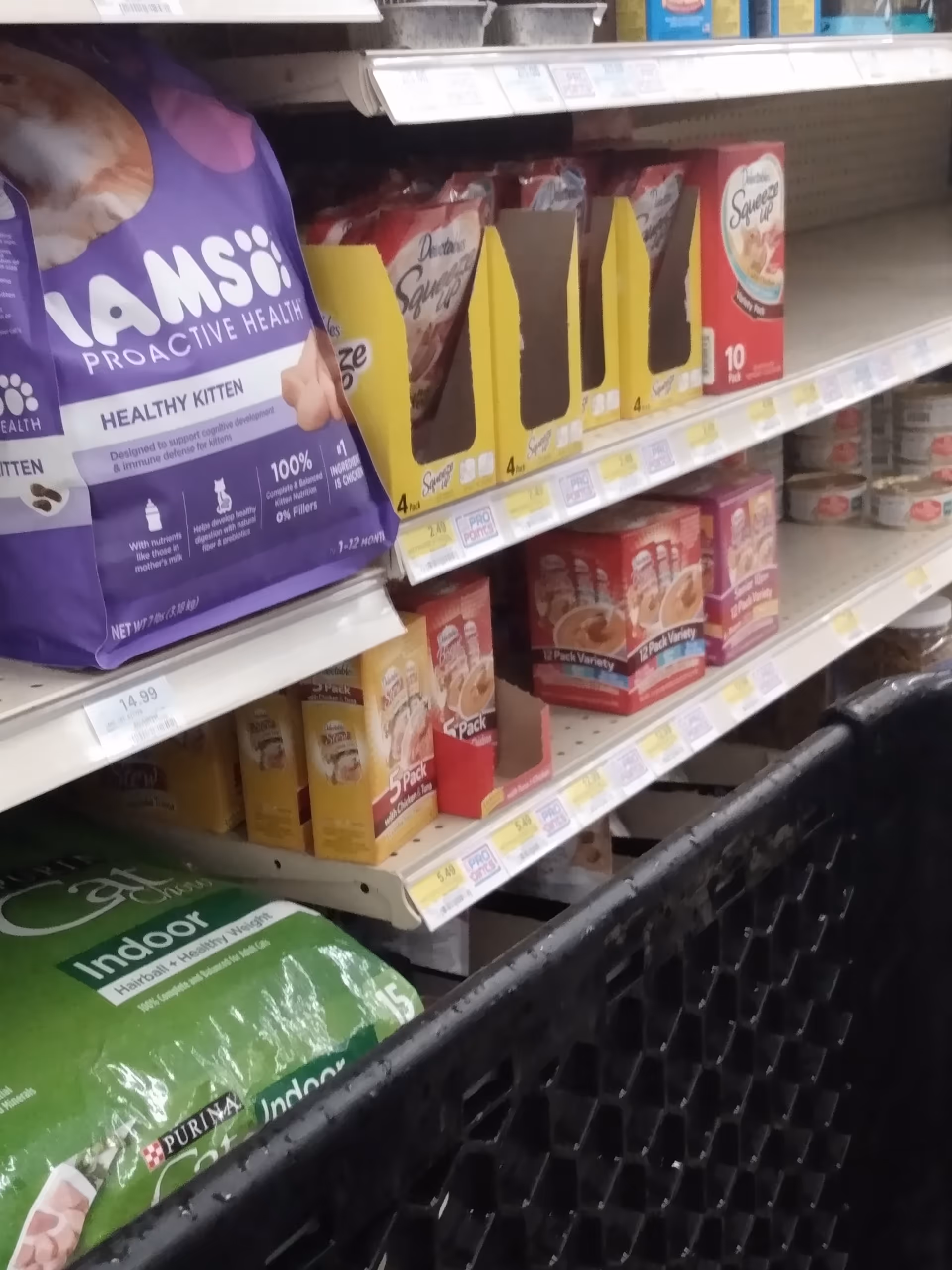 Store aisle with pet food and litter bags on shelves and shopping cart.