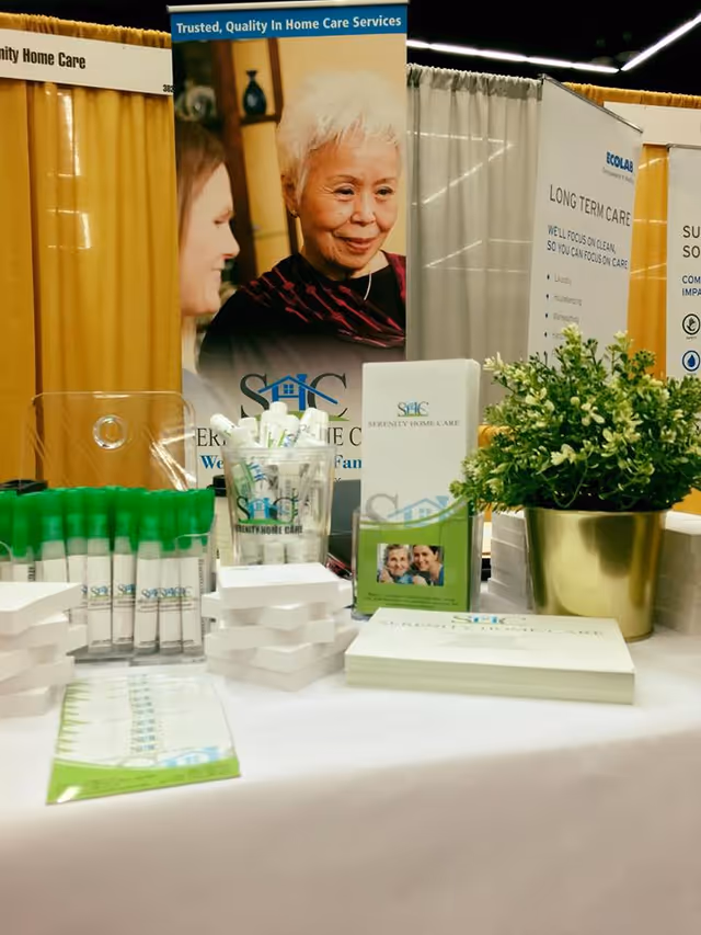 Trade show booth displays for Serenity Home Care with banners, brochures, and a potted plant.
