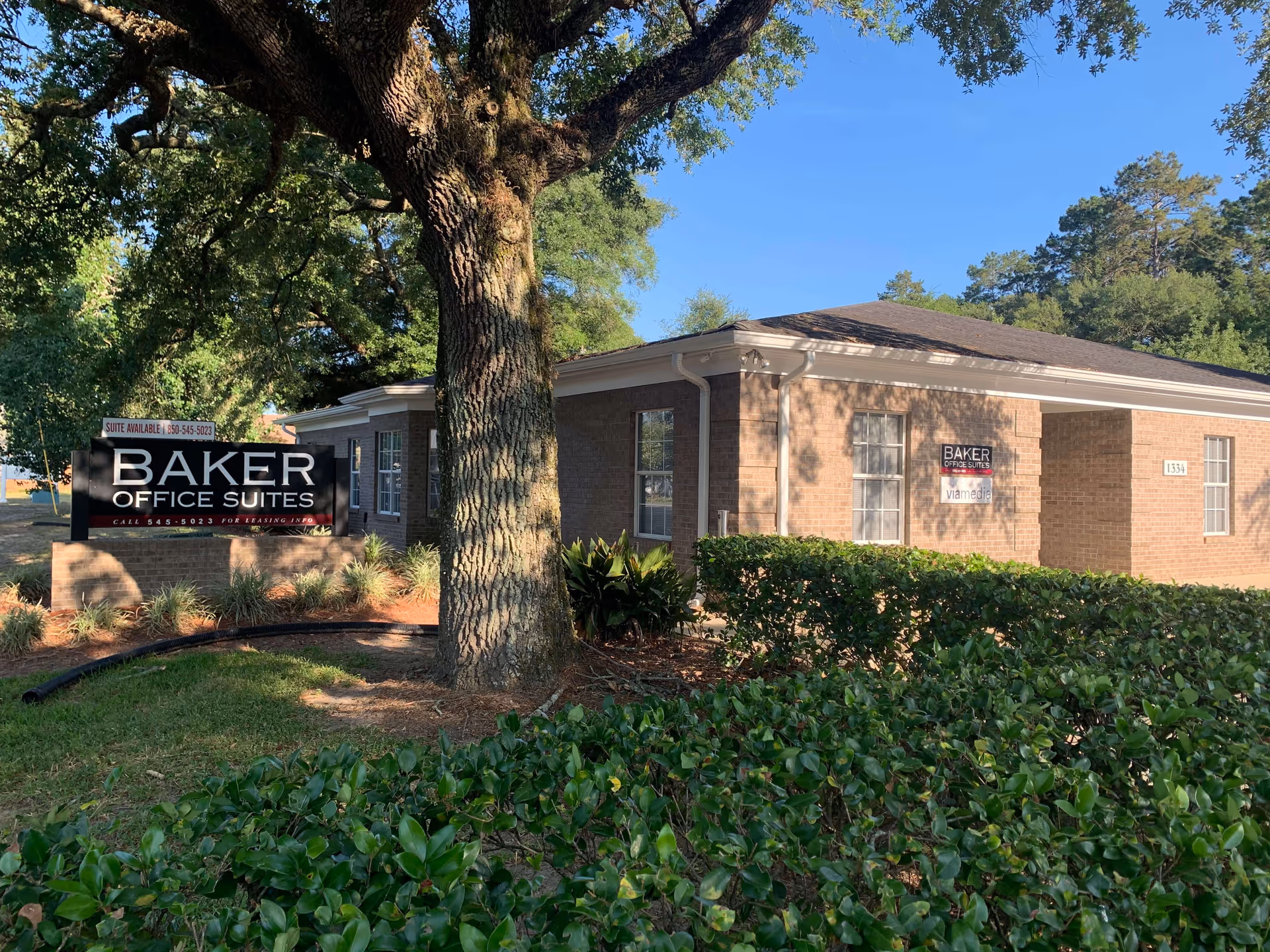 Brick office building exterior with a Baker Office Suites sign beside trees and hedges.