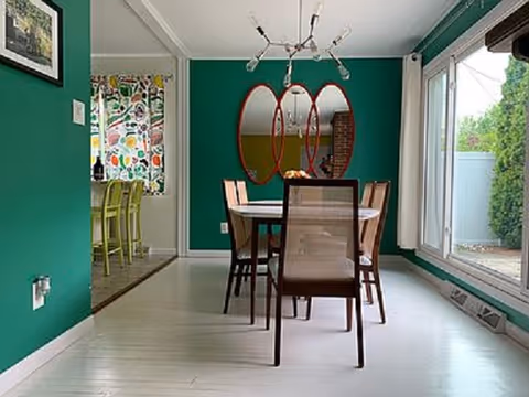Bright dining room with teal walls, a glass table, wooden chairs, and large windows.