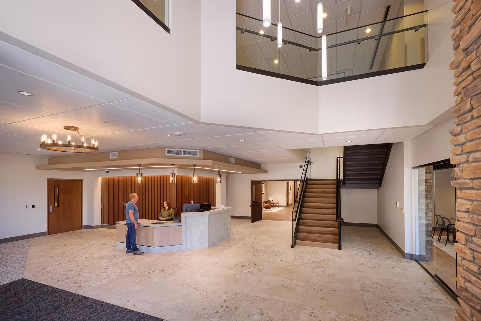Bright lobby interior with curved reception desk, staircase, and glass railing on a two-level atrium.