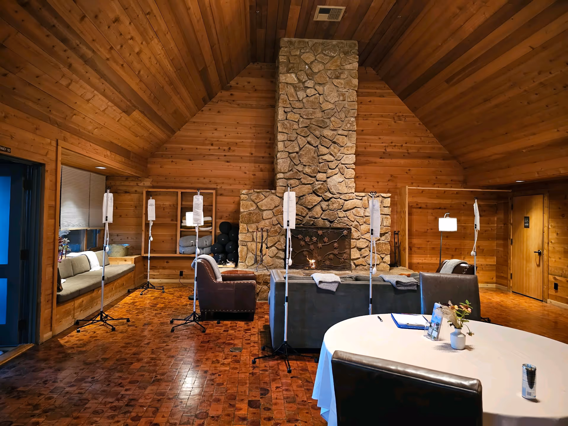 A rustic, wood-paneled living room with a stone fireplace, sofas, and IV stands.