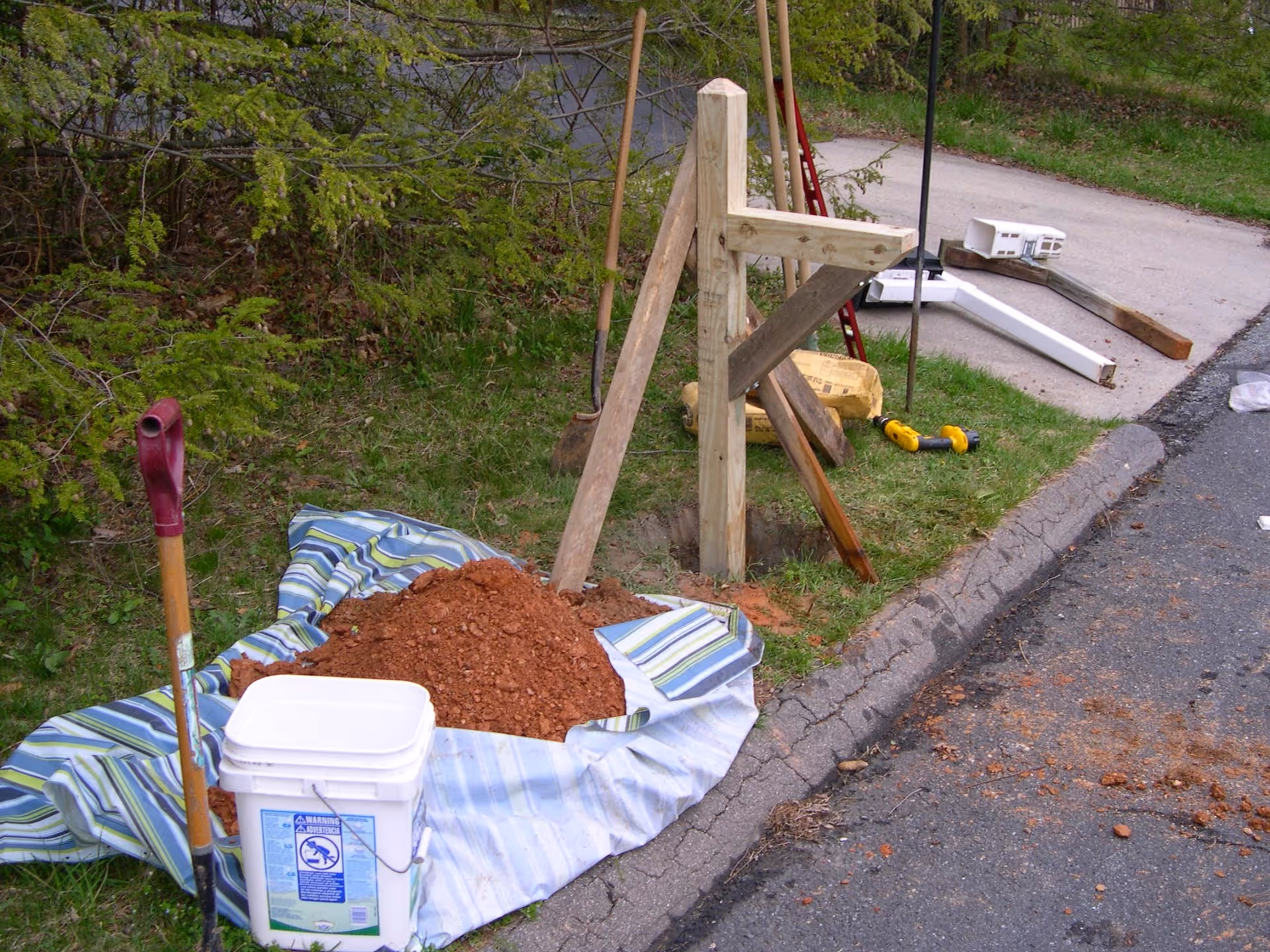Outdoor construction scene with dirt pile, shovels, wooden framework along a curb.