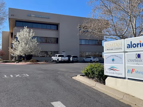 Exterior view of a beige office building with a parking lot and entrance sign.