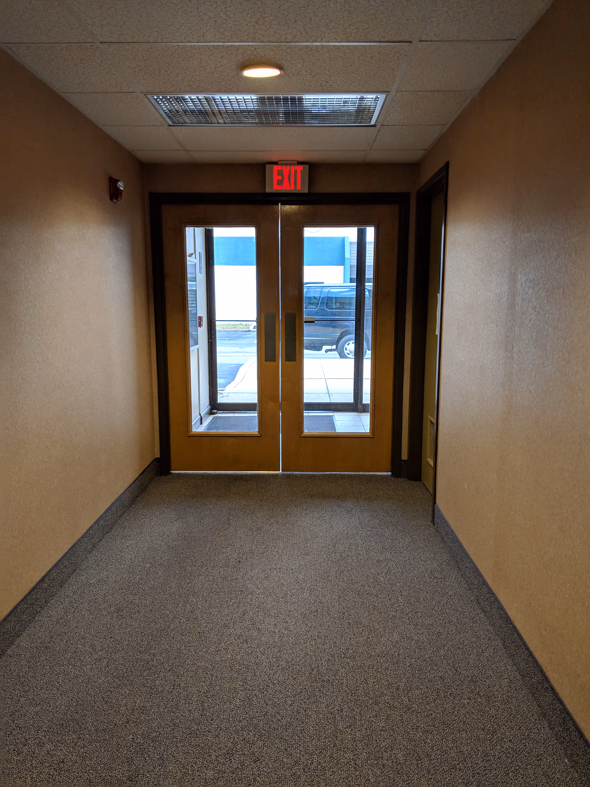 Interior hallway with double glass doors and an illuminated exit sign.