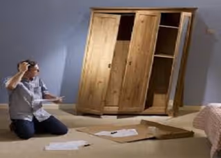 Person kneels beside an open wardrobe lying on the bedroom floor with scattered papers.