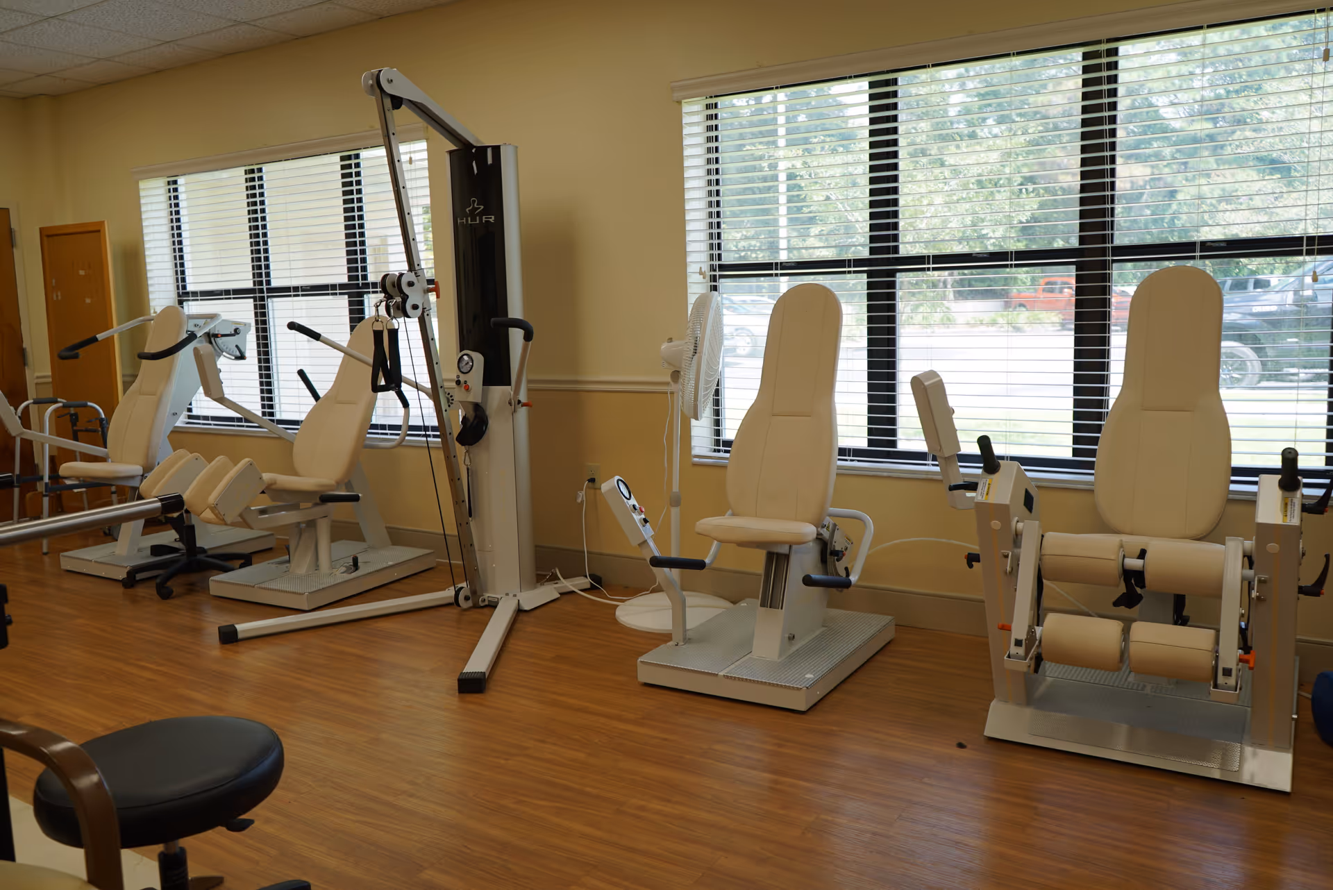 Senior living facility exercise room with white gym equipment and large windows.