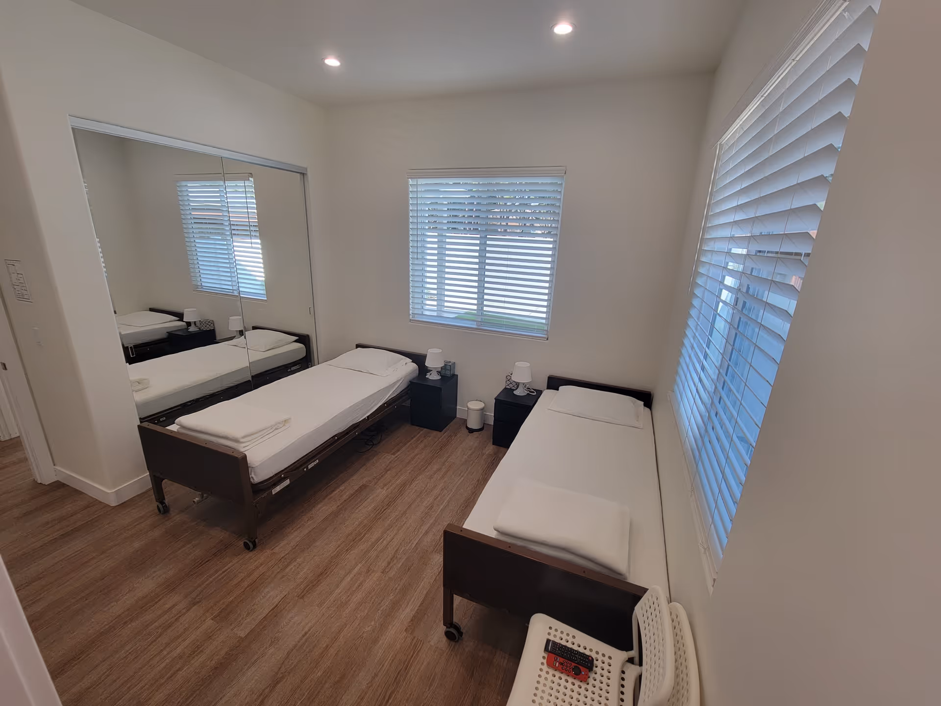 Two twin beds in a clean, bright bedroom with windows and mirrored closet doors.