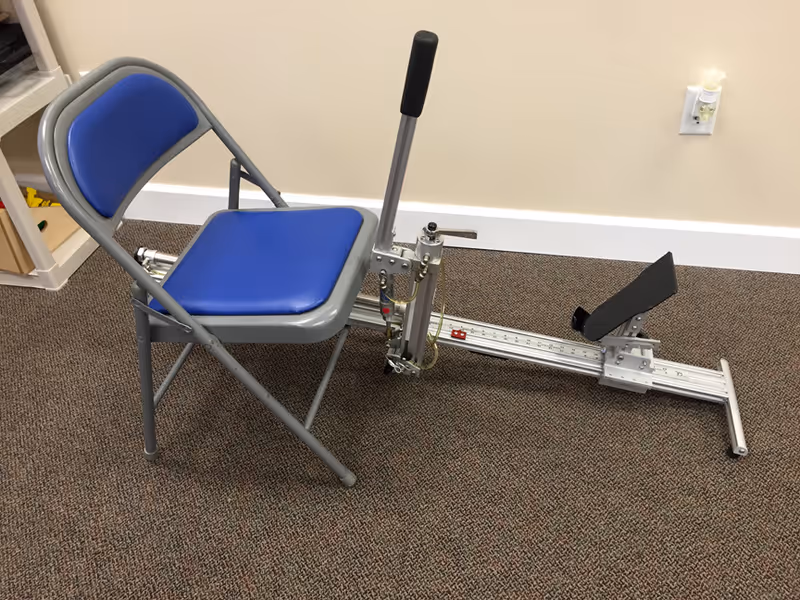 Blue padded chair with a long metal therapy device attached in a carpeted interior.