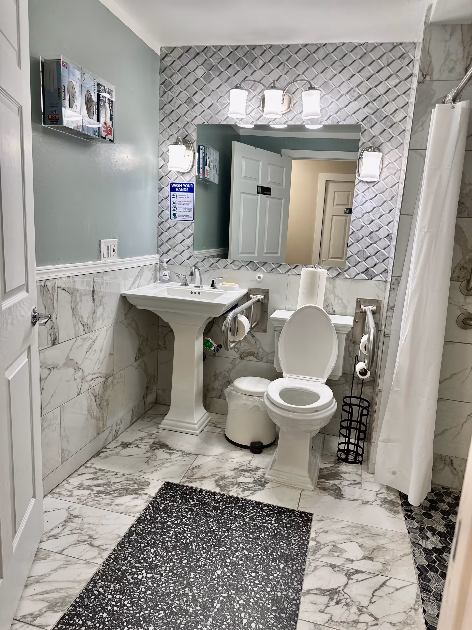 Marble-tiled bathroom with pedestal sink, toilet, mirror, and shower curtain.