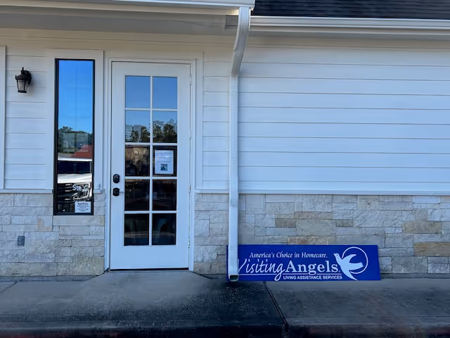 White building entrance with glass door and blue Visiting Angels sign.