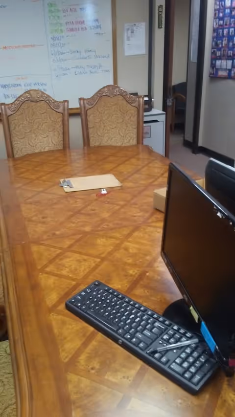 A long wooden conference table with monitor, keyboard, and whiteboard in a meeting room.