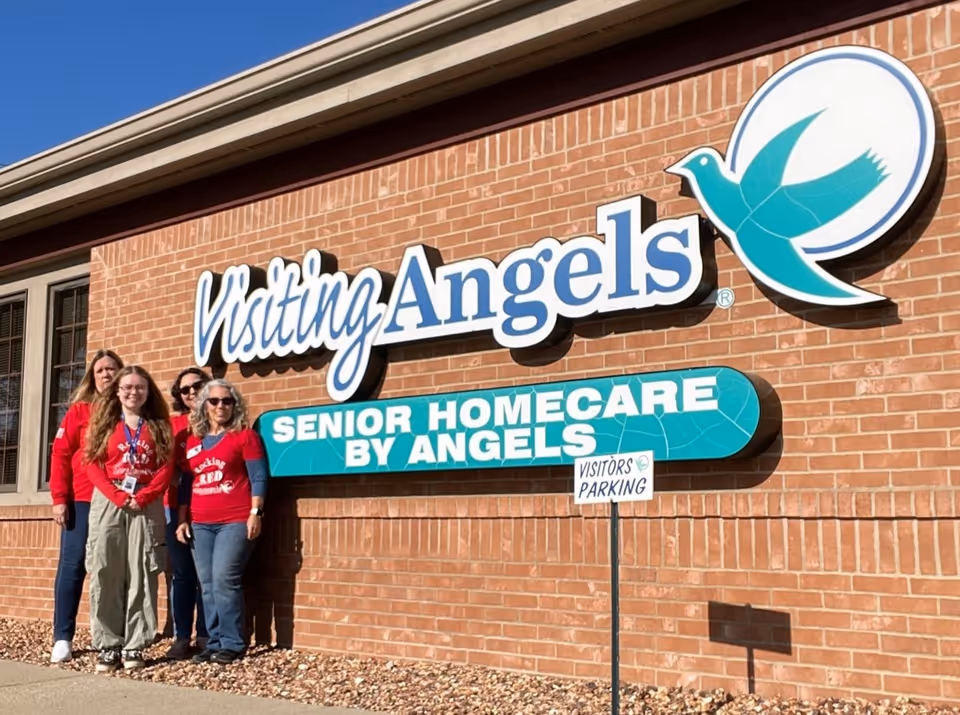 Exterior brick building with Visiting Angels sign and several people posing in front.