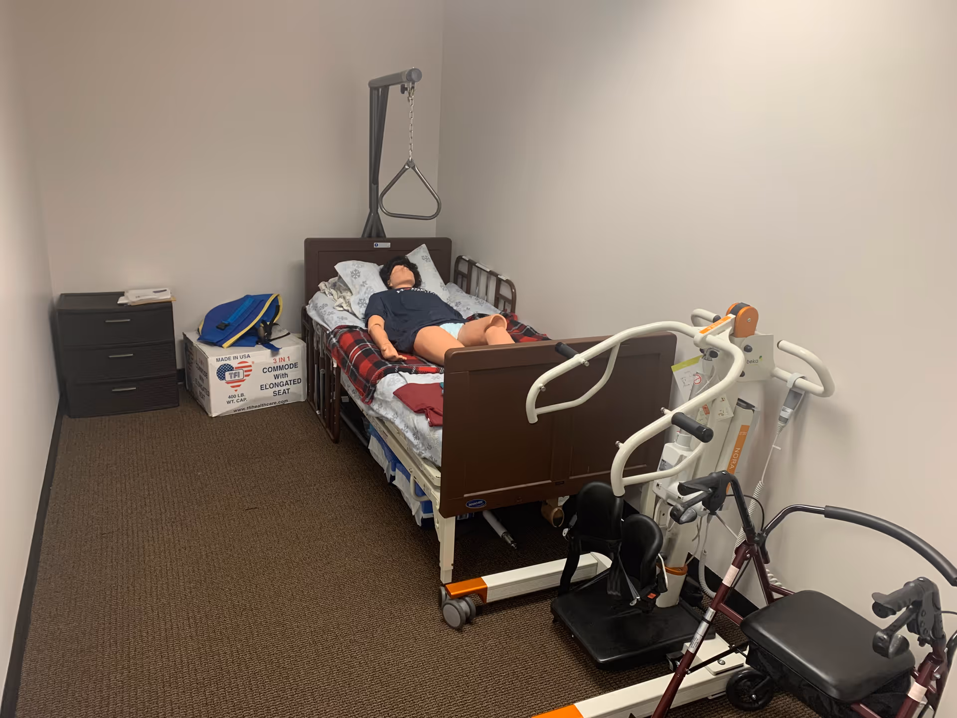 Resident rests in a hospital-style bed with mobility equipment in a small private room.