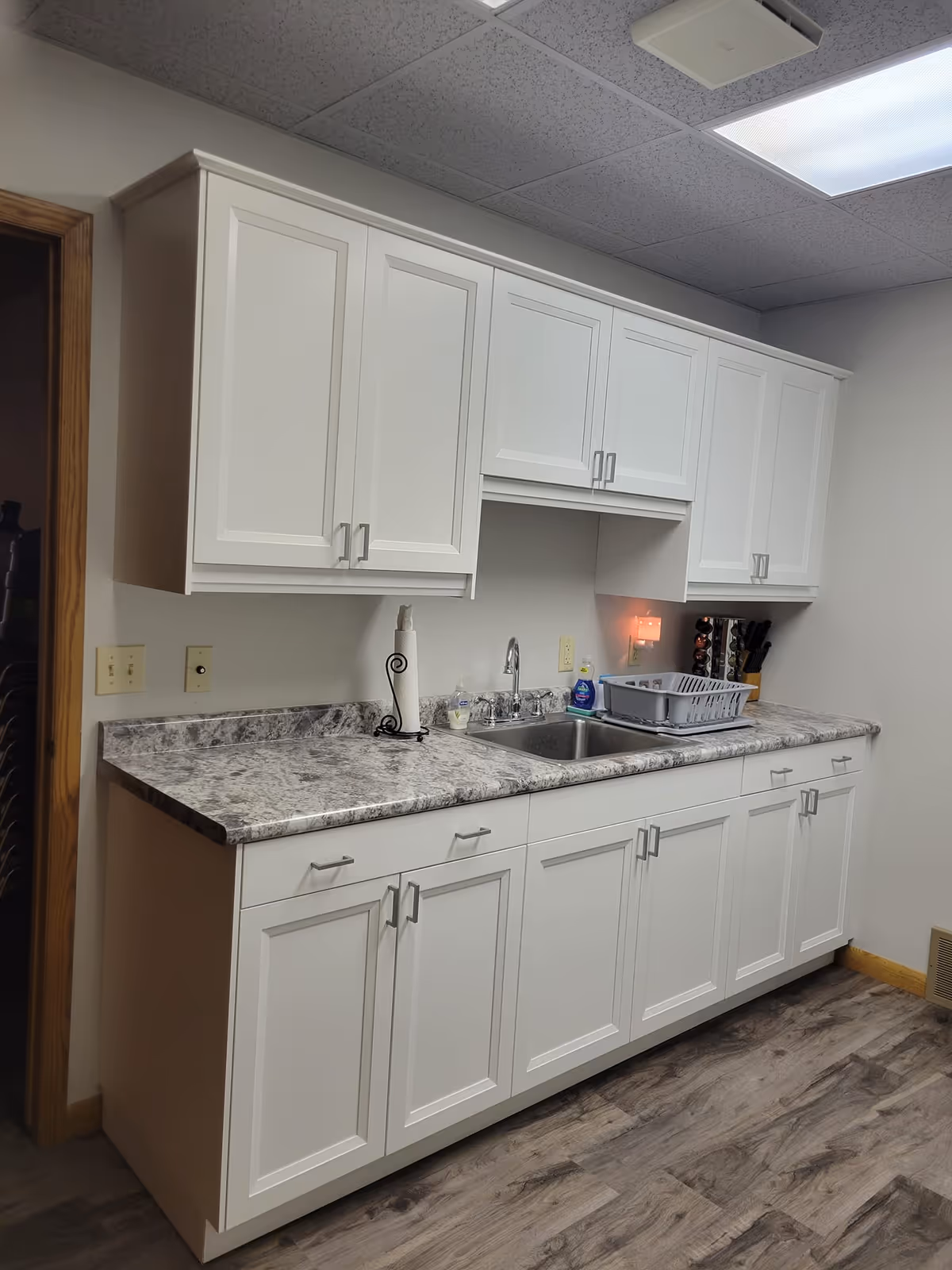 White kitchen cabinets surround a marble countertop with a sink and dish rack.