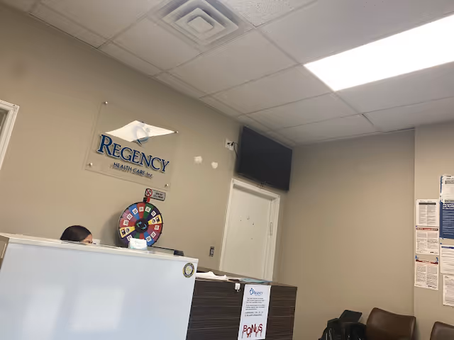 Reception area with Regency Health Care sign, a spinning wheel, front desk, and a wall-mounted TV.