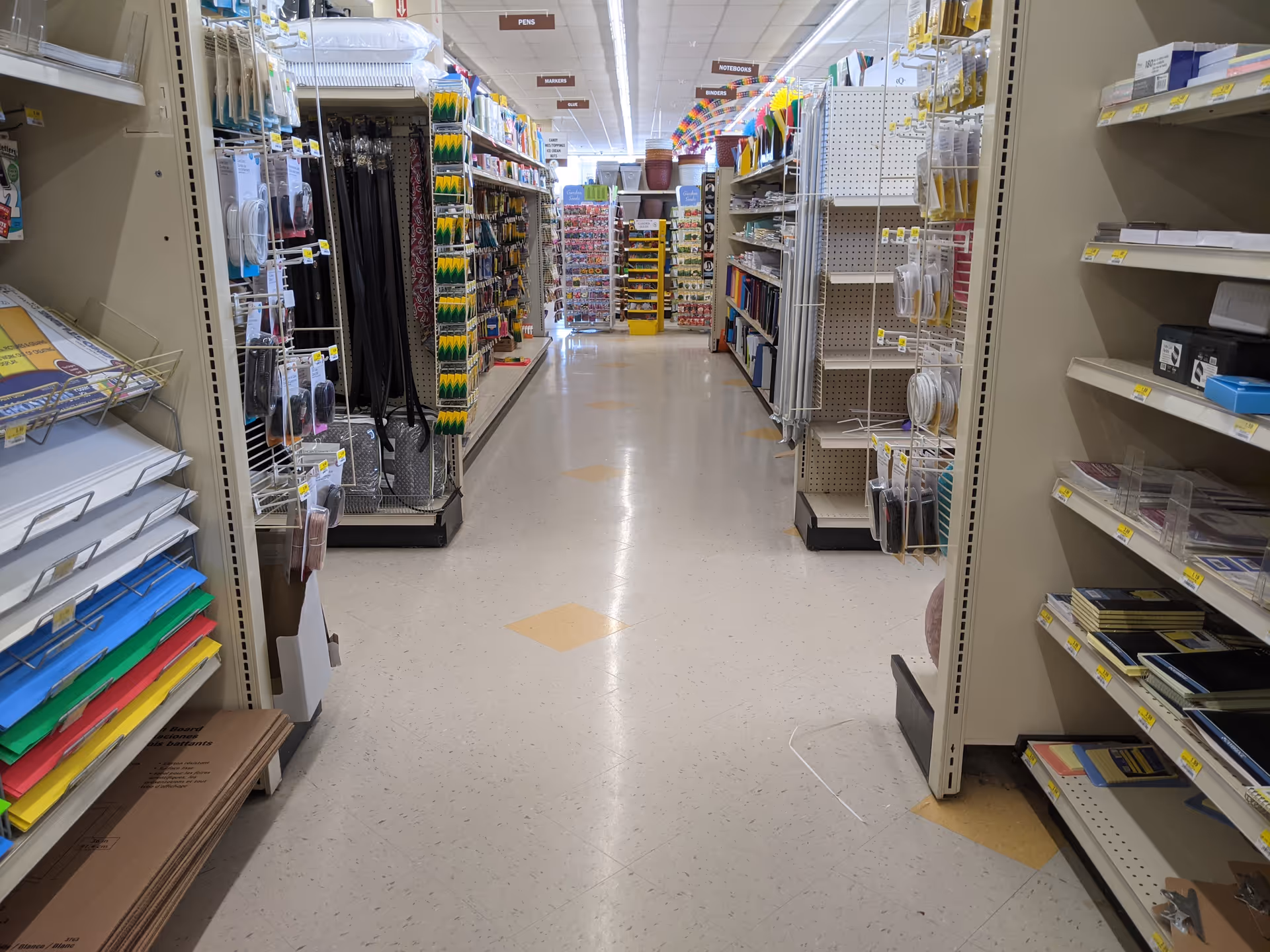 Aisle view inside Discount Drug Mart showing tall shelves stocked with assorted supplies.