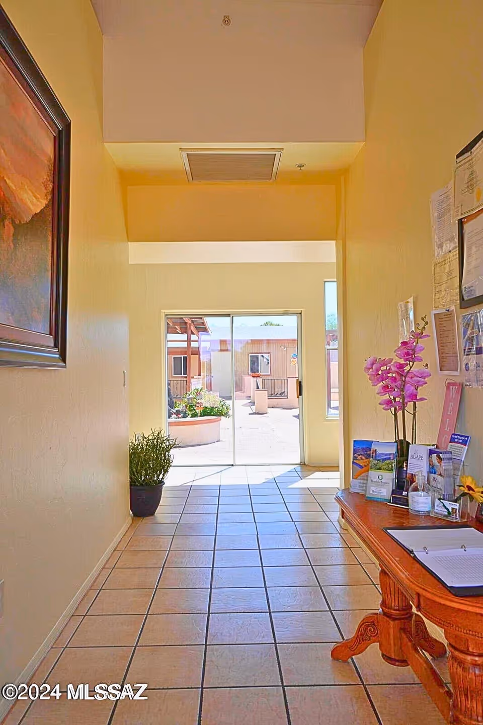 Bright hallway lobby with tiled floor, reception table, brochures, and glass exit door.