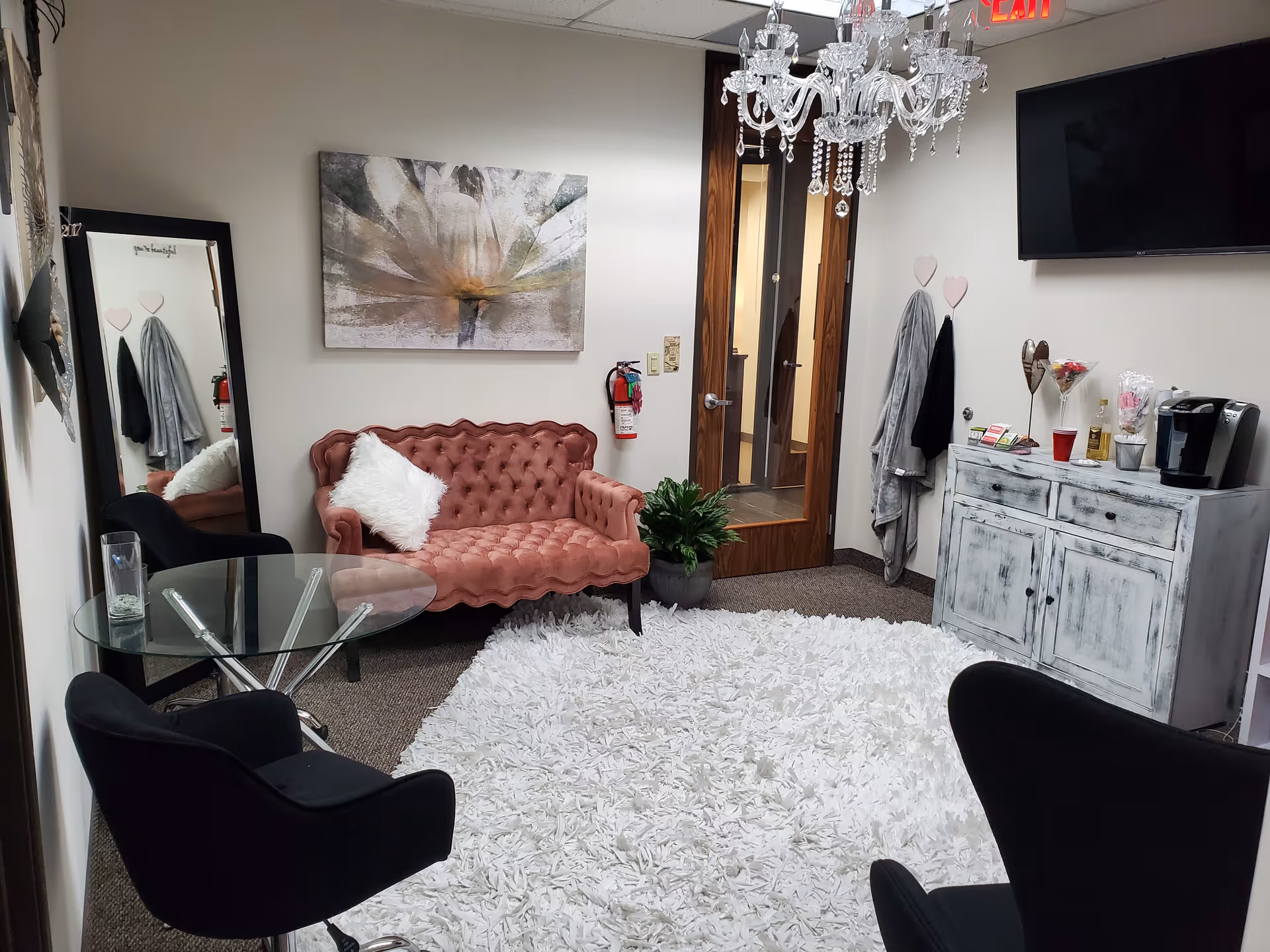 Cozy lounge with pink tufted sofa, glass table, chandelier, and white shag rug.