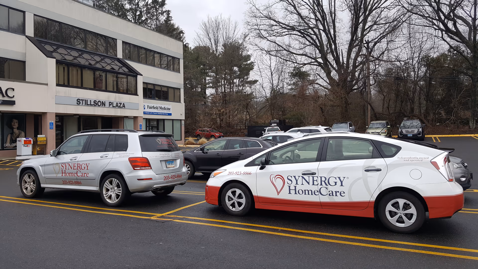 Two Synergy HomeCare cars parked in front of a medical office building named Stillson Plaza.
