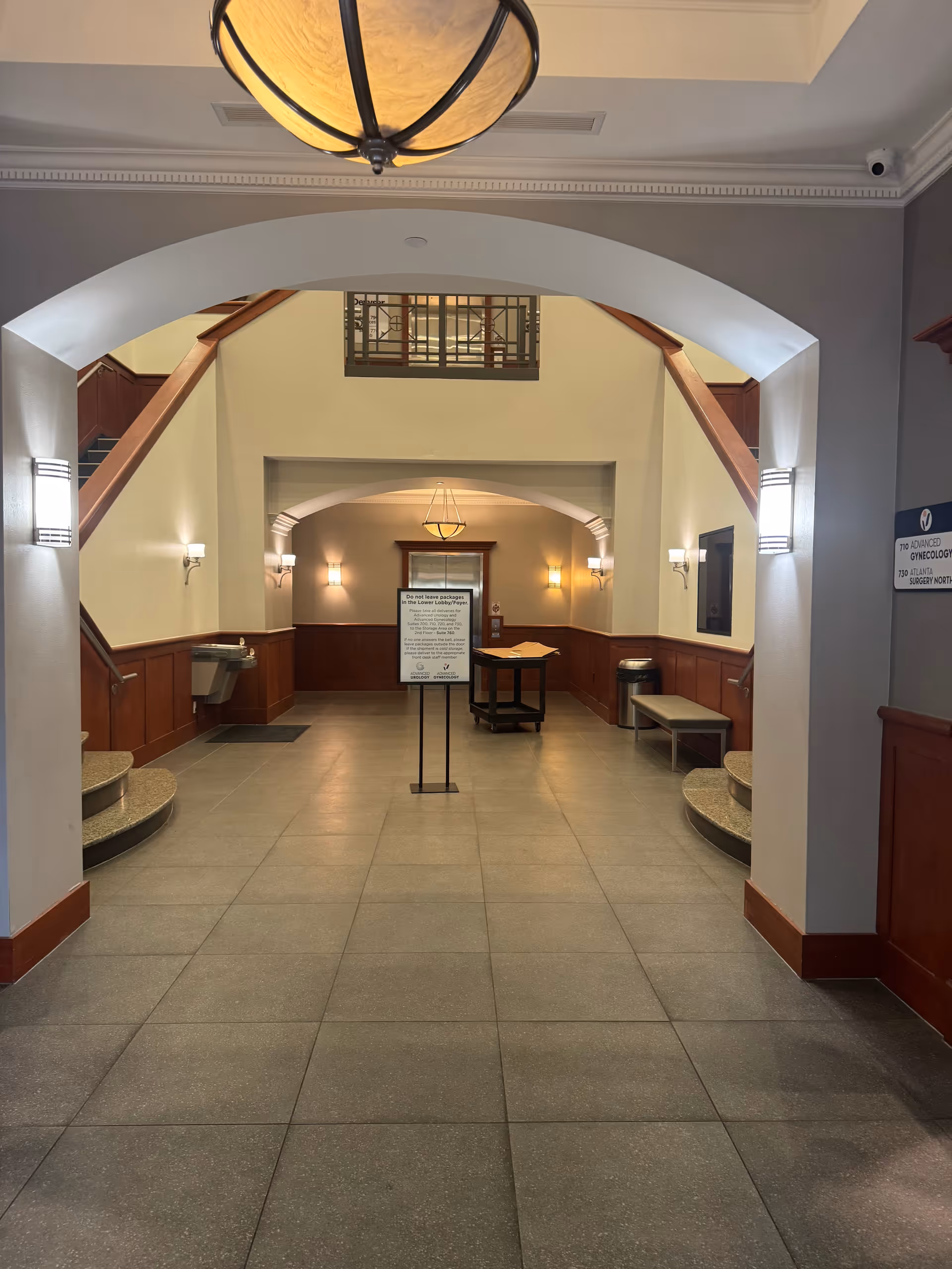 Interior lobby with arches, staircases on both sides, a central sign, and benches.