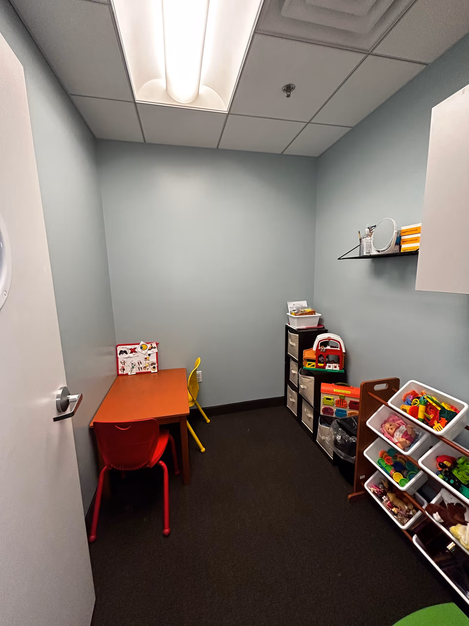 Small sensory play room with toy shelves, colorful chairs, and a table.