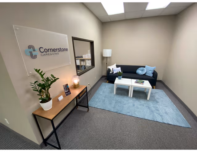 Interior lobby area with Cornerstone Caregiving sign, sofa, coffee tables, lamp, and plants.