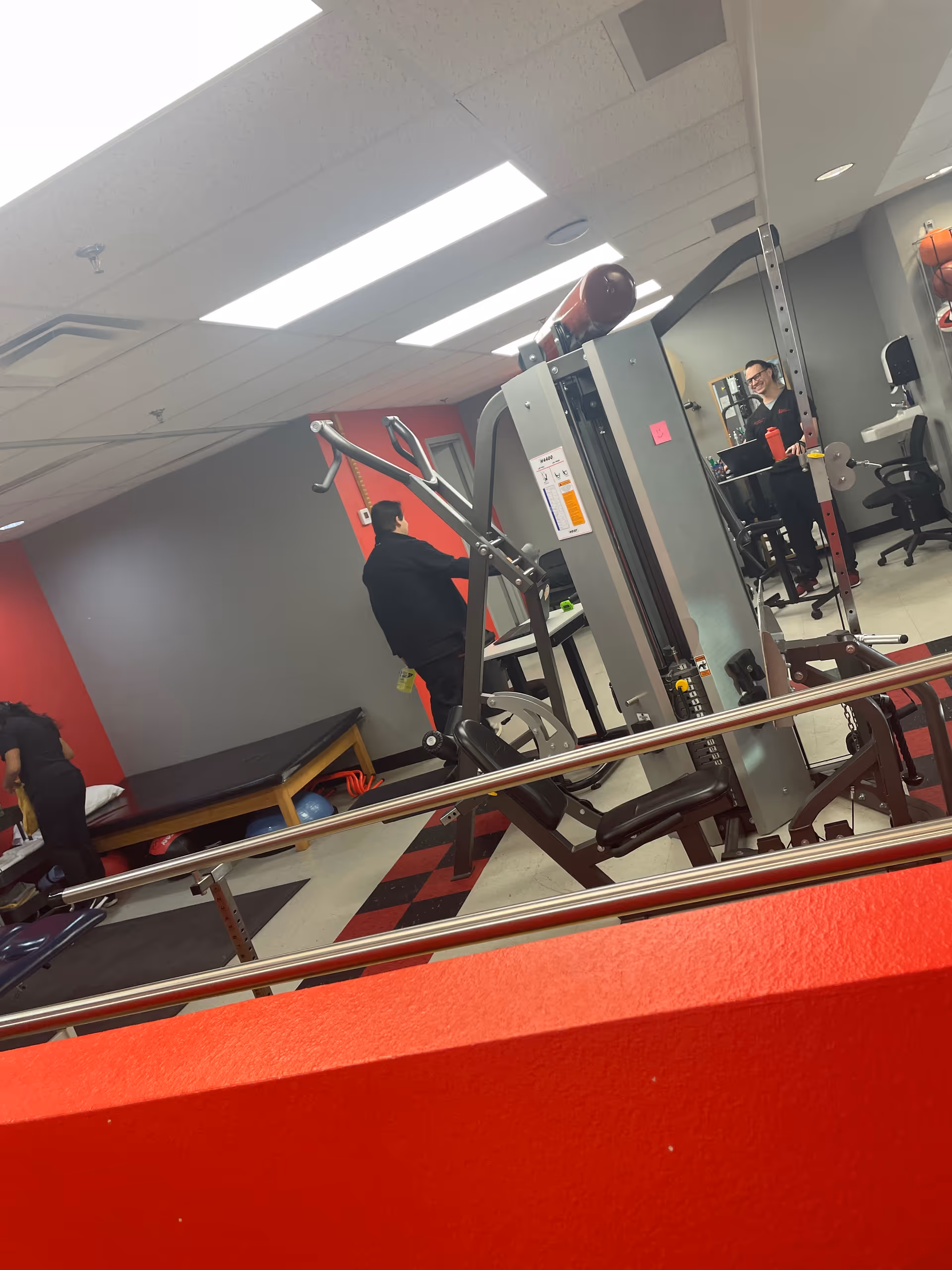 An indoor rehabilitation gym with weight machines and staff nearby.