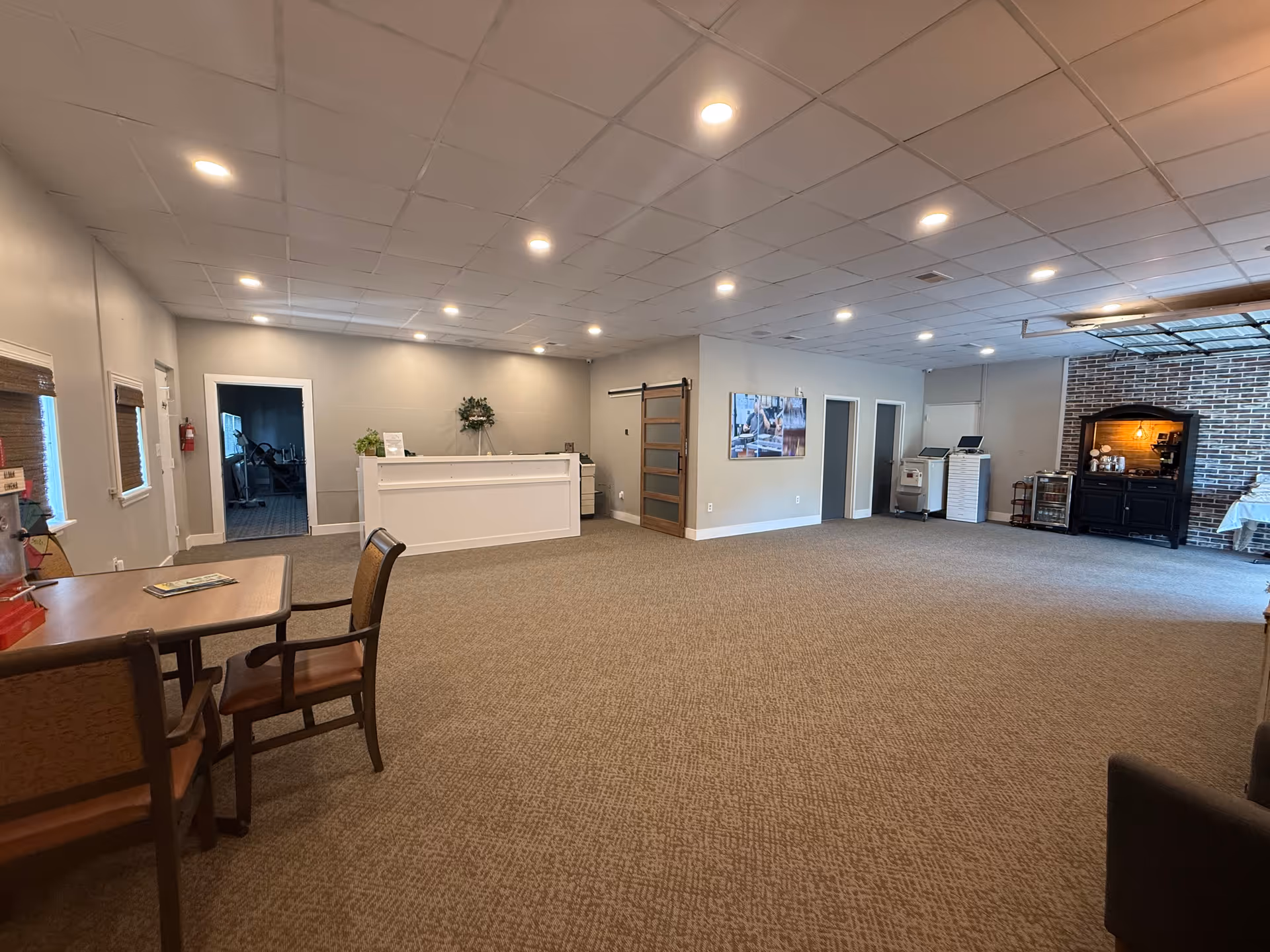 Spacious senior living lounge with reception desk, seating, and a brick fireplace.