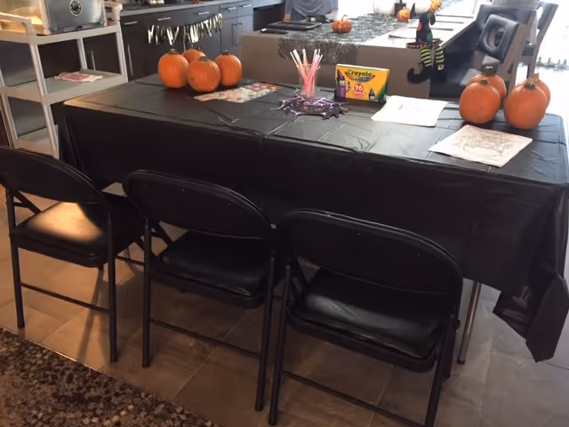 Dining table with black cloth, pumpkins, and Halloween decorations in a kitchen area.