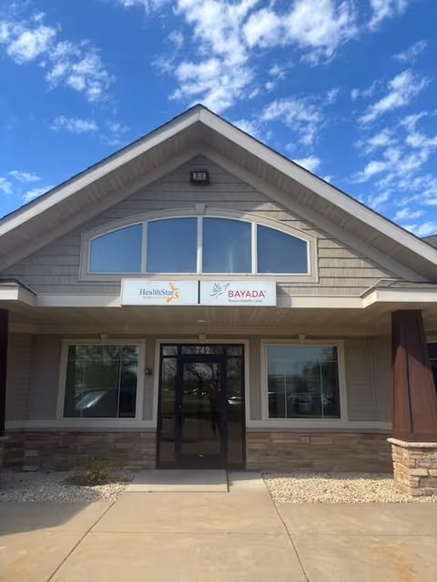 Front of BAYADA Pediatrics facility with sign, glass doors, stone accents, and blue sky.