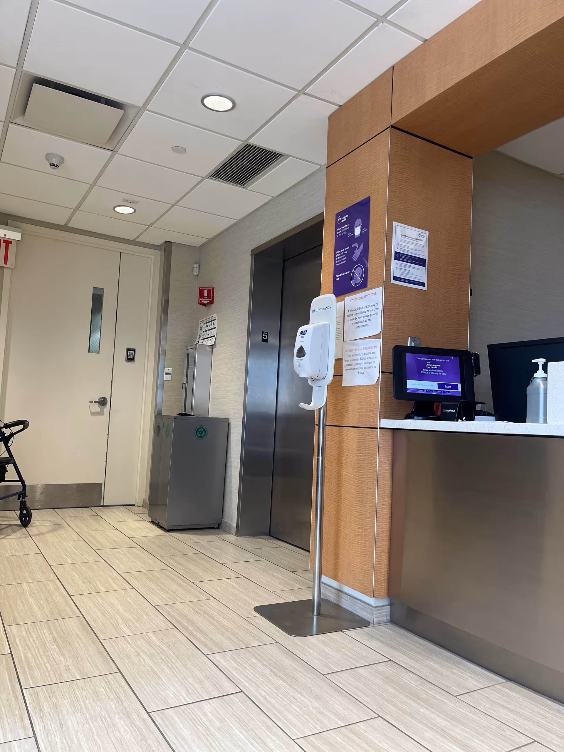 Interior hallway of a medical facility with an elevator, reception desk, and doorway.