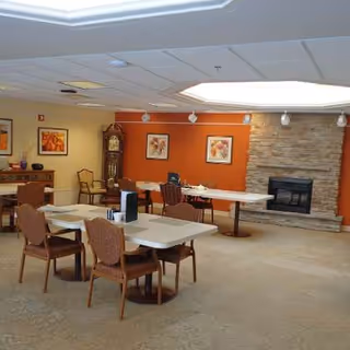 Senior living facility dining room with tables, chairs, orange wall, and a stone fireplace