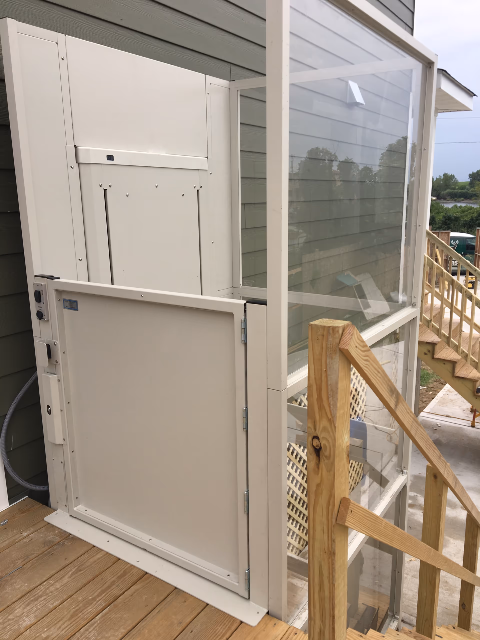 Exterior equipment enclosure beside a wooden deck and glass-walled structure attached to siding