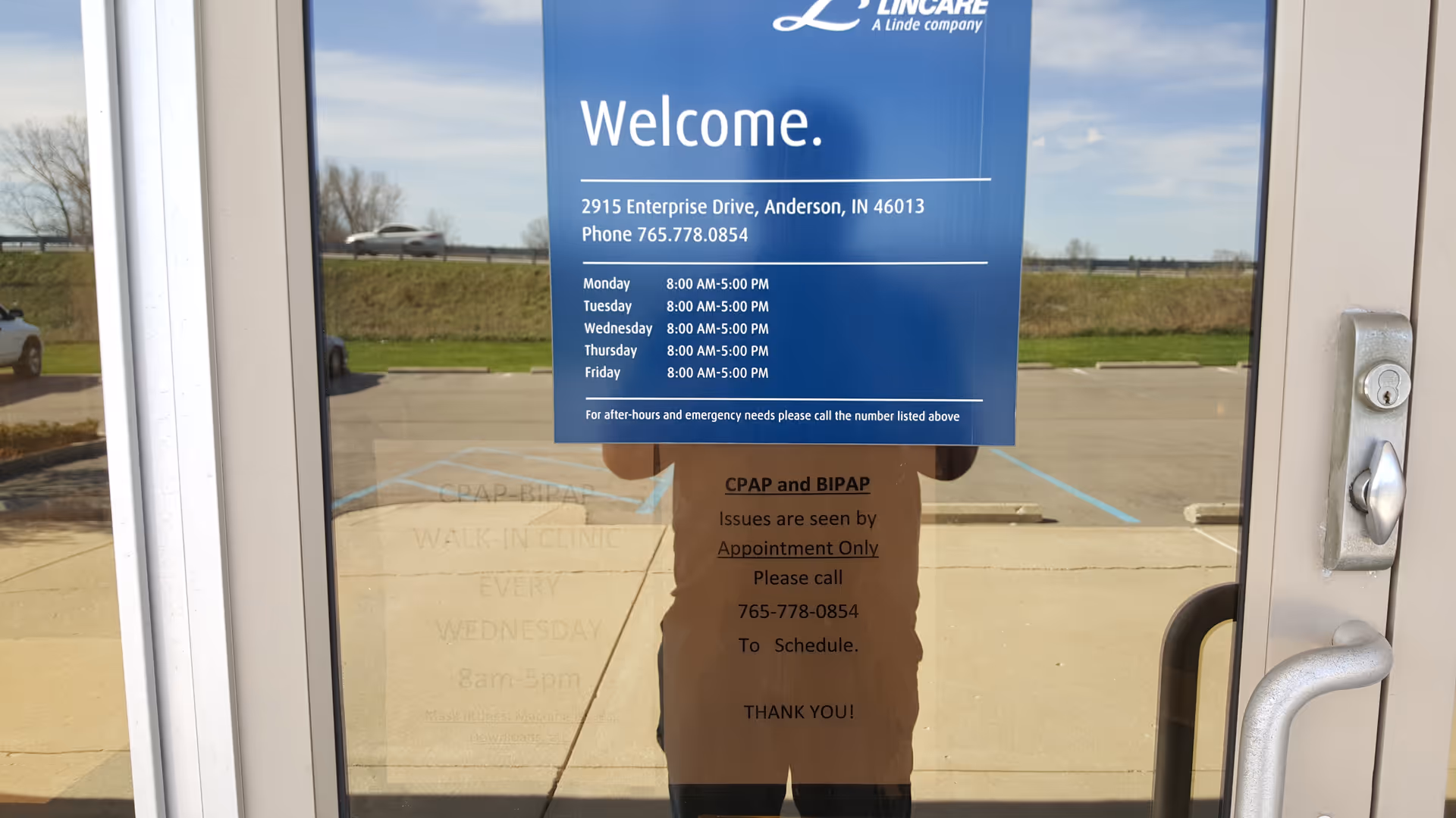 Blue welcome sign on glass door with facility information and parking outside.