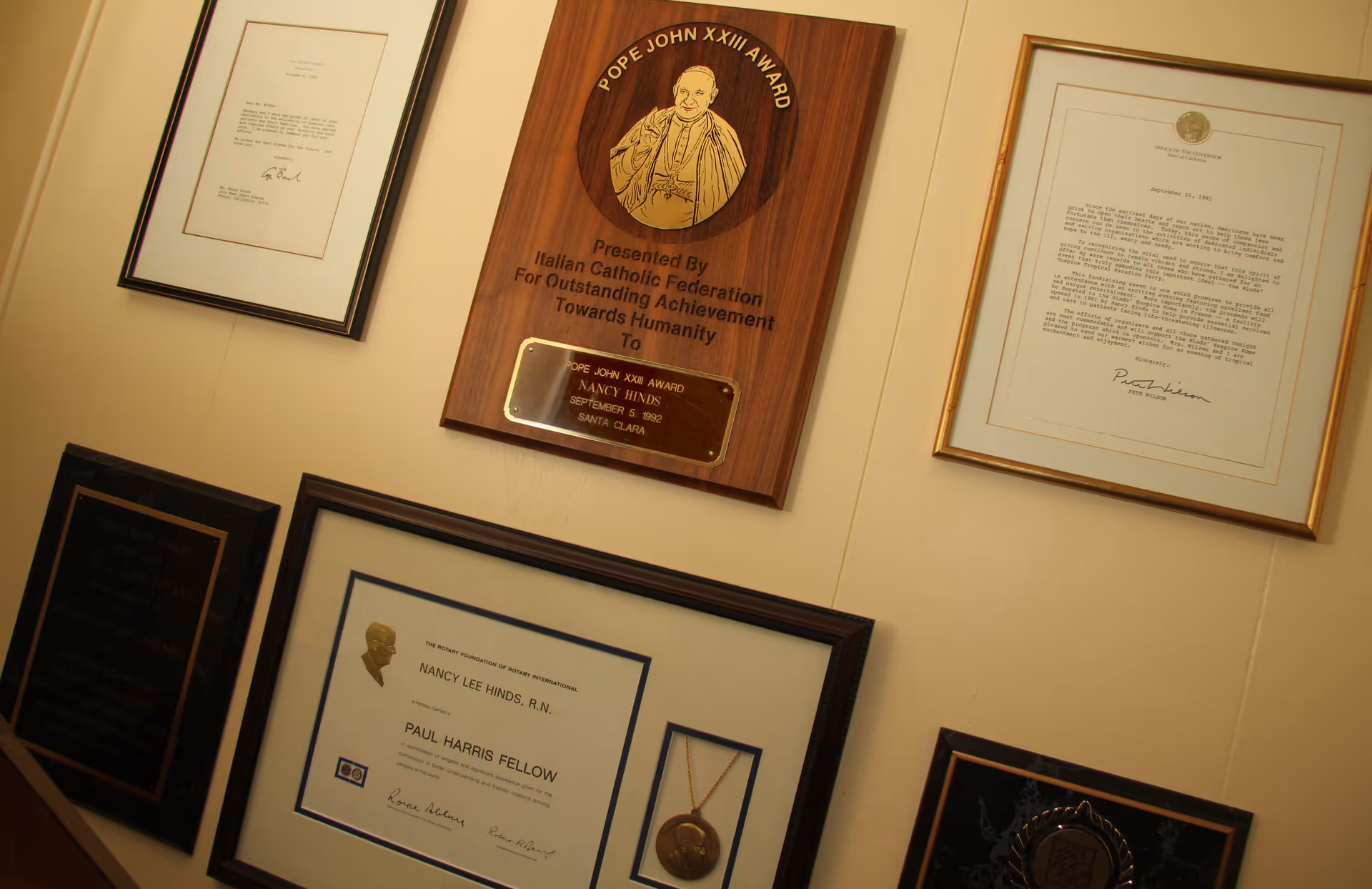 Wall with framed awards and certificates displayed in a senior care facility hallway